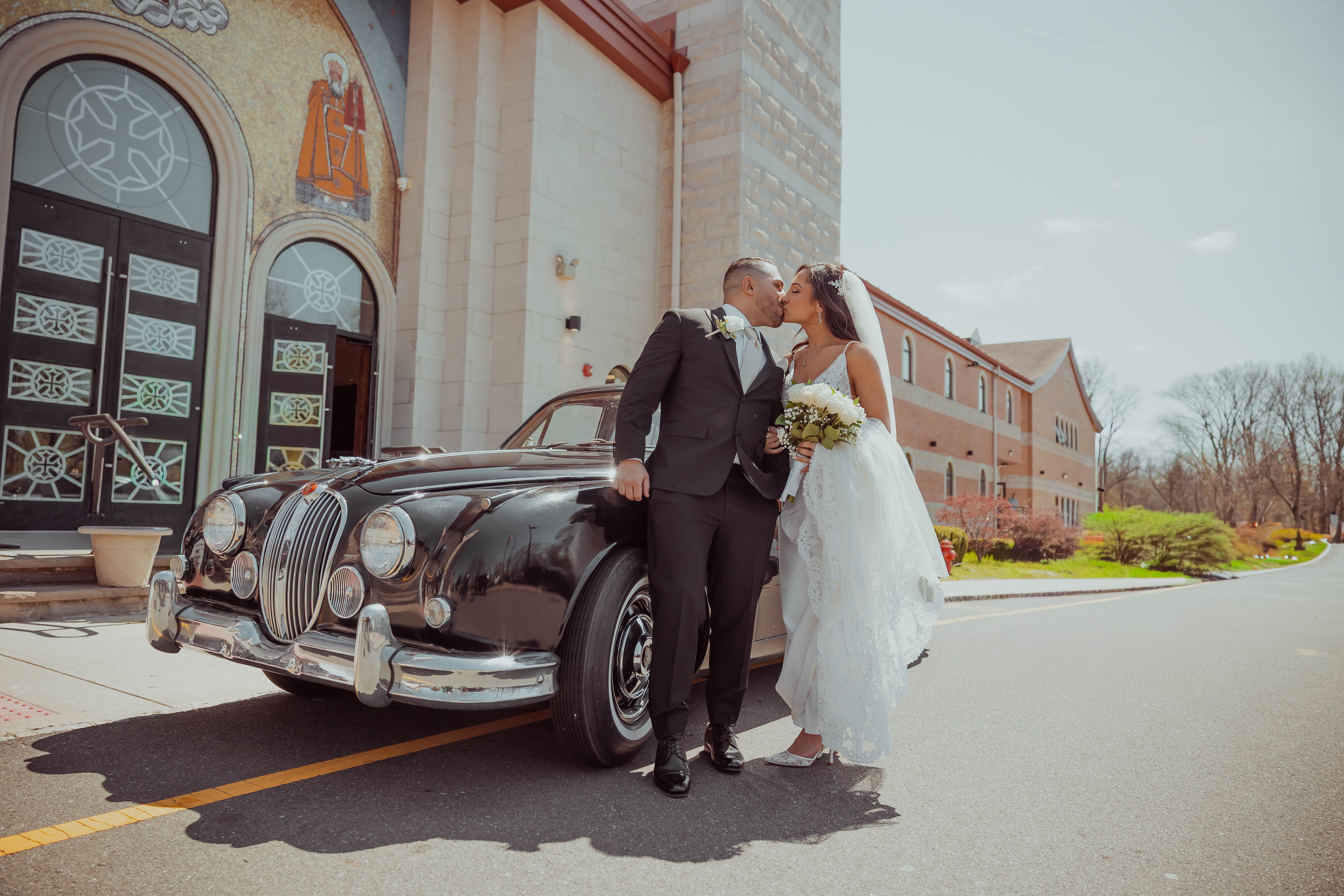 Christina and Mike kiss beside a vintage Jaguar outside St. Mina Coptic Orthodox Church in Holmdel, New Jersey